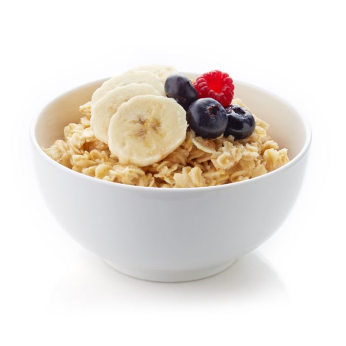 Bowl of wholesome breakfast cereal with bananas, blueberries, and raspberries on white background.