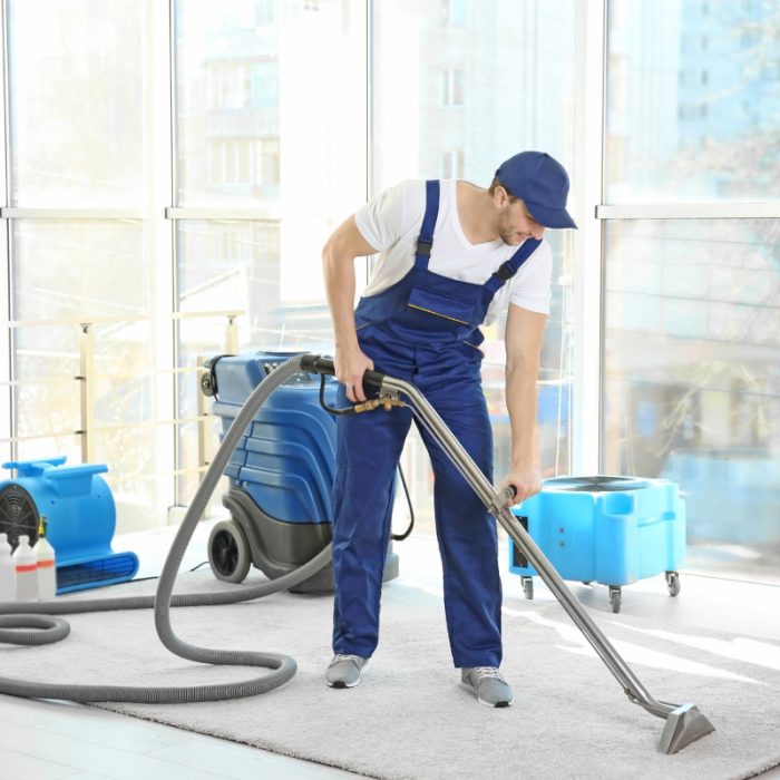 Man in uniform using a professional vacuum cleaner on a bright room's carpet.