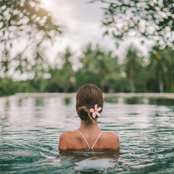 Woman relaxing in a serene natural pool with a flower in her hair, embodying tranquility.